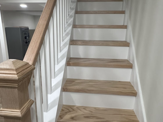 Finished basement staircase with wood treads, white painted risers, and wooden handrail