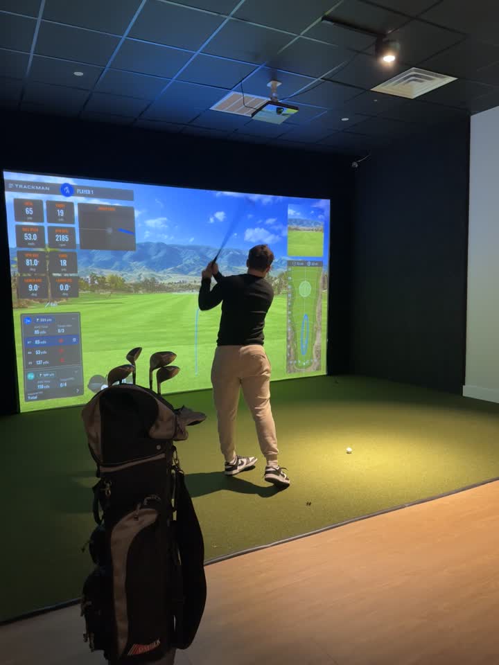 A full golf swing in a simulator bay at Chip & Birdie's in Mountainside NJ, with the projection screen ahead, turf underfoot and the black tile ceiling above